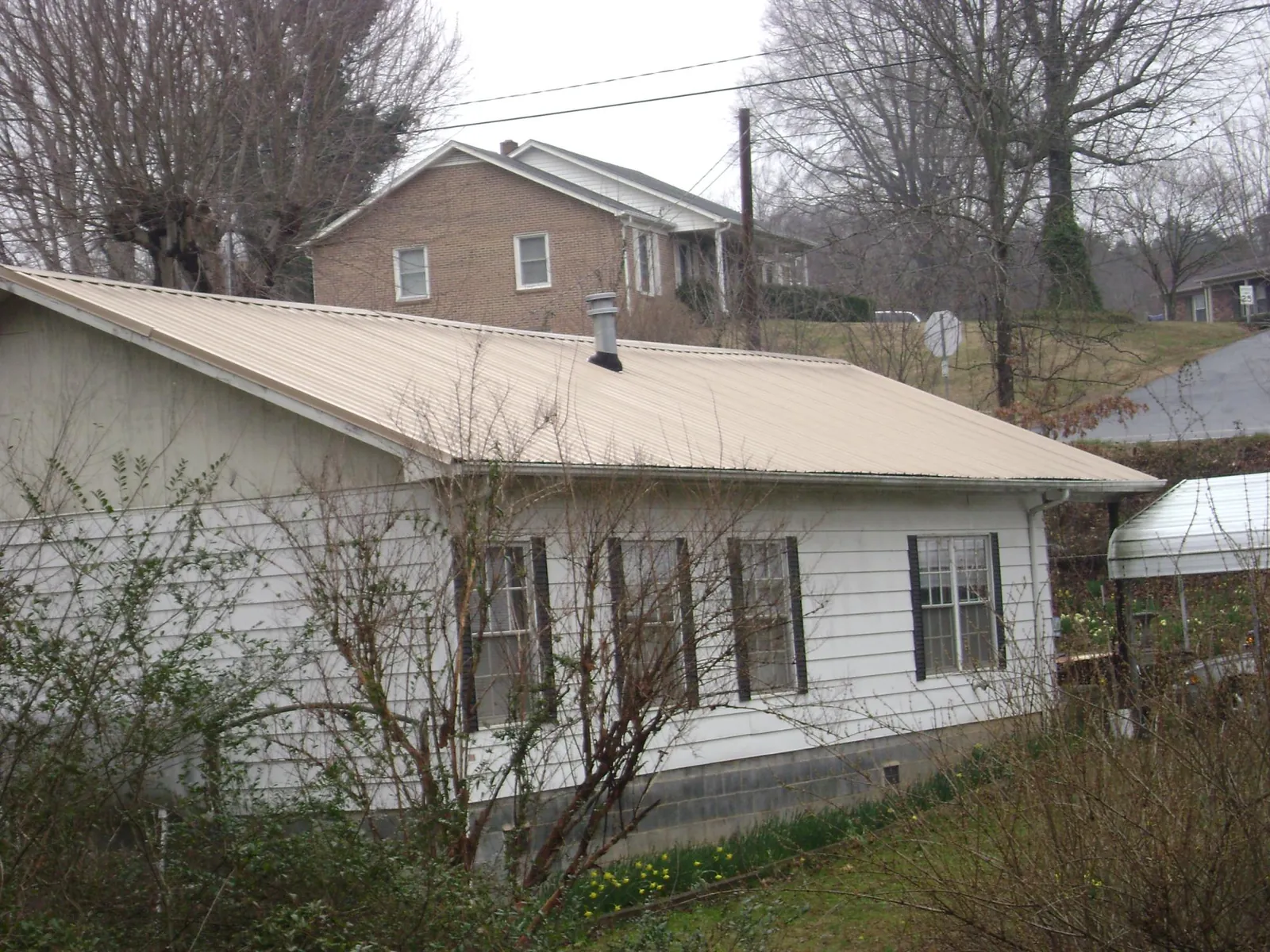 Tan metal roof on a white sided house set into a hillside — Commercial Roofing by Roofing Brothers in Hermosa Beach